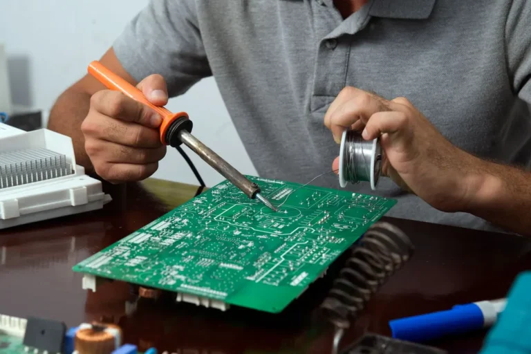 Manos de un técnico reparando con soldador la placa electrónica de un electrodoméstico