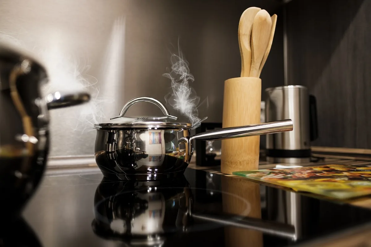 Olla de acero inoxidable con vapor sobre una placa de cocina de cristal negro