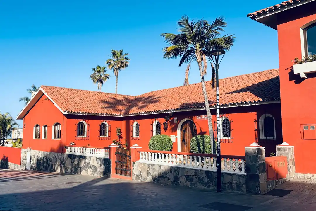Casa de tejas rojas con muros de colores y palmeras bajo un cielo azul