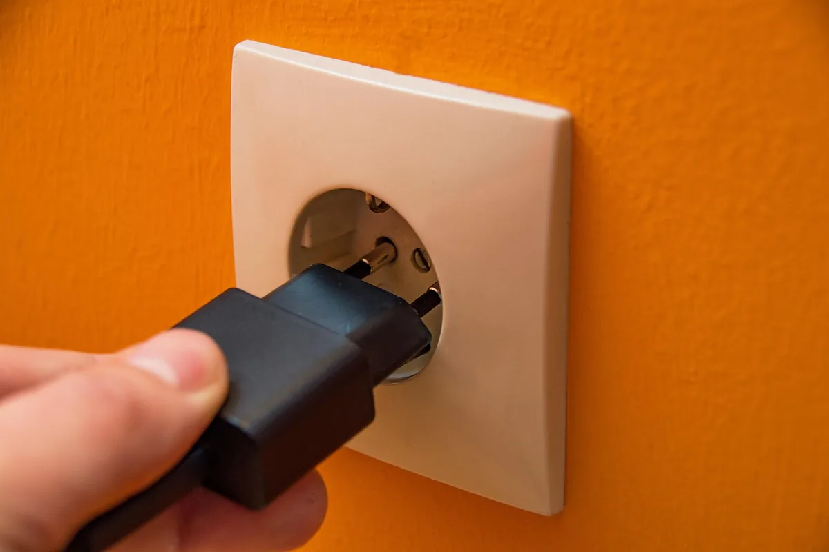 Mano enchufando un cable negro en un enchufe de pared