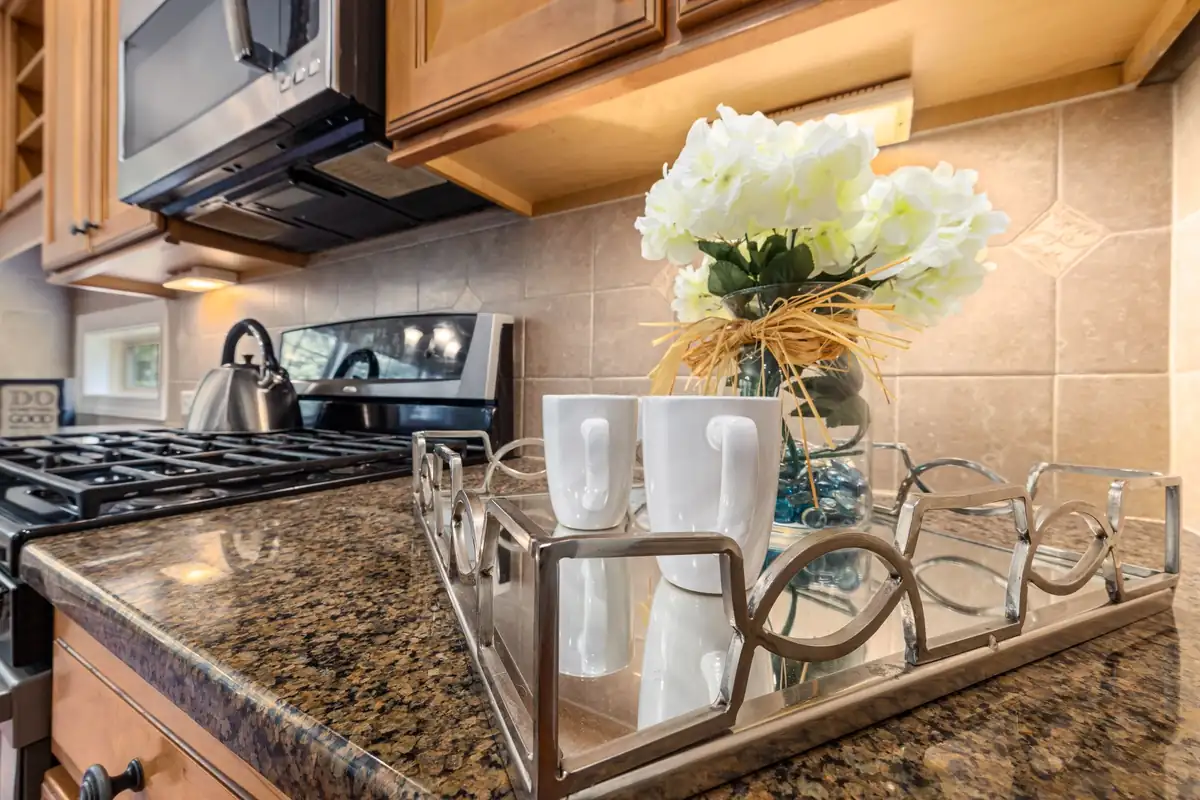 Encimera de granito de una cocina con una bandeja con dos tazas blancas y flores, y una placa de gas con un hervidor