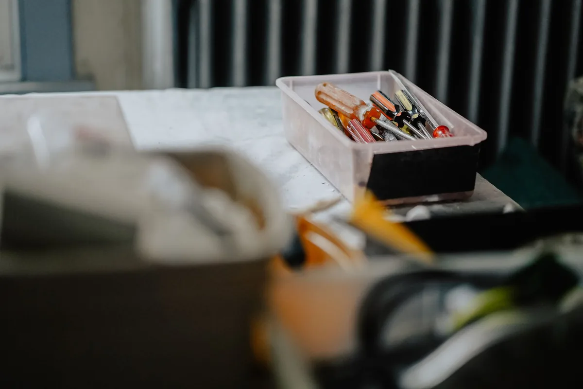 Caja de plástico con destornilladores de mango naranja, rojo y negro sobre una mesa de trabajo