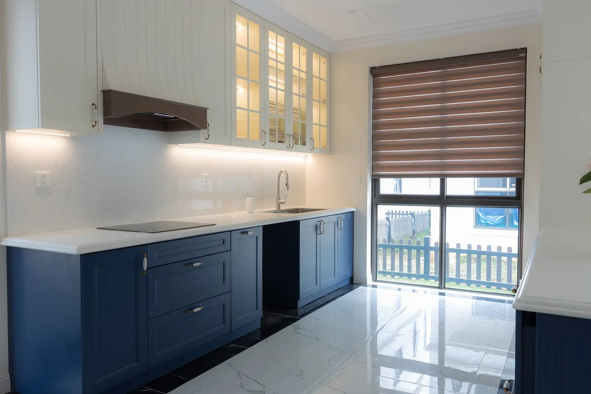Cocina con armarios azules, encimera blanca y placa de inducción, bajo una campana con frontal de madera