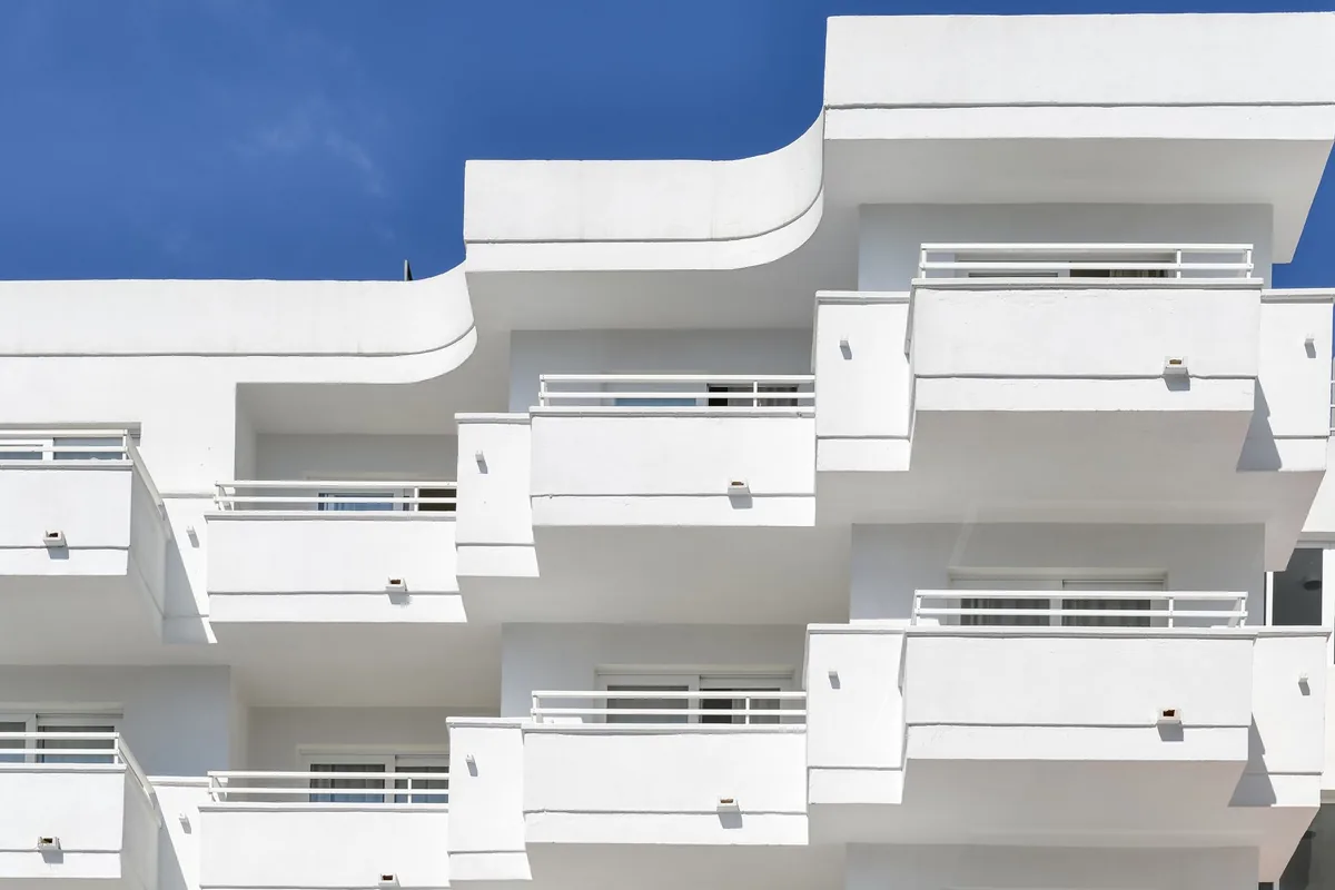 Fachada blanca de un bloque de viviendas con balcones escalonados y barandillas blancas, bajo un cielo azul