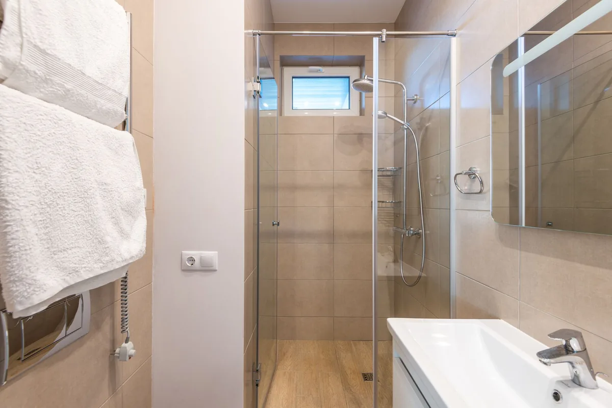Cuarto de baño con ducha de mampara de cristal, lavabo blanco y toallas blancas colgadas