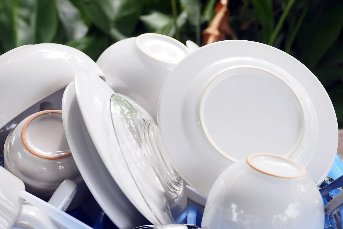 Platos, cuencos y tazas blancos limpios apilados en un escurridor