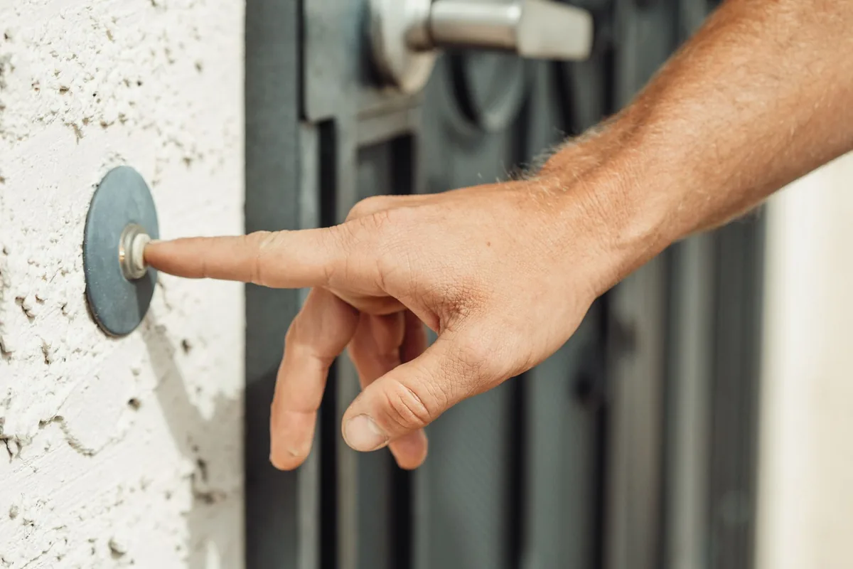 Mano pulsando el timbre junto a la puerta de una vivienda