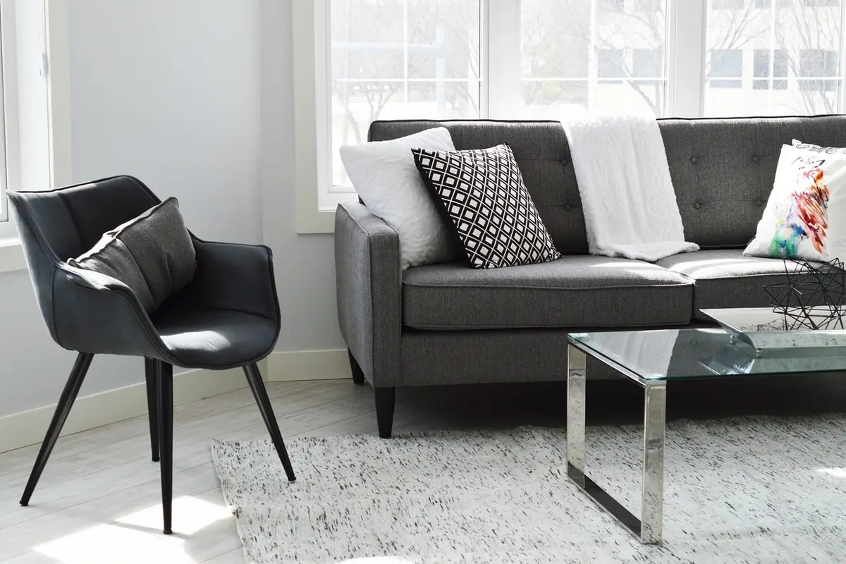 Salón luminoso con un sofá gris y un sillón junto a unos ventanales