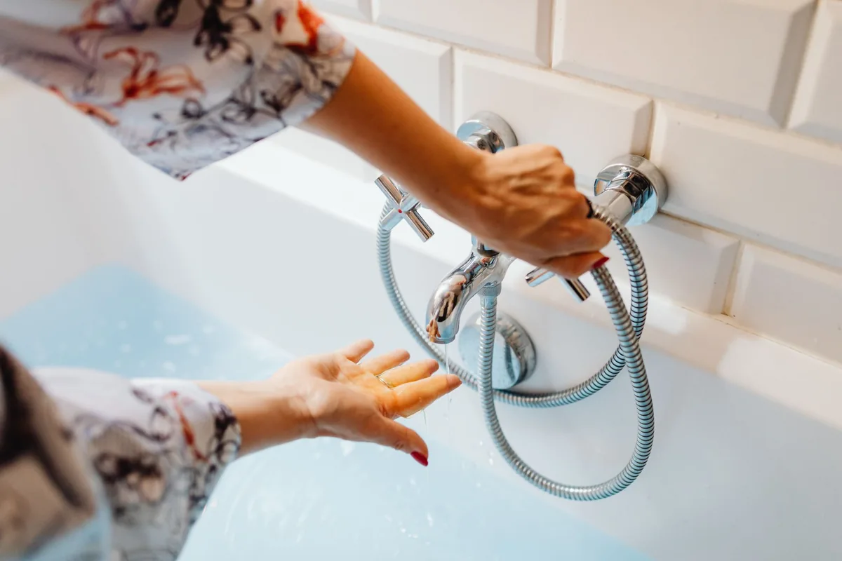 Mano probando con la palma el agua que cae del grifo de una bañera