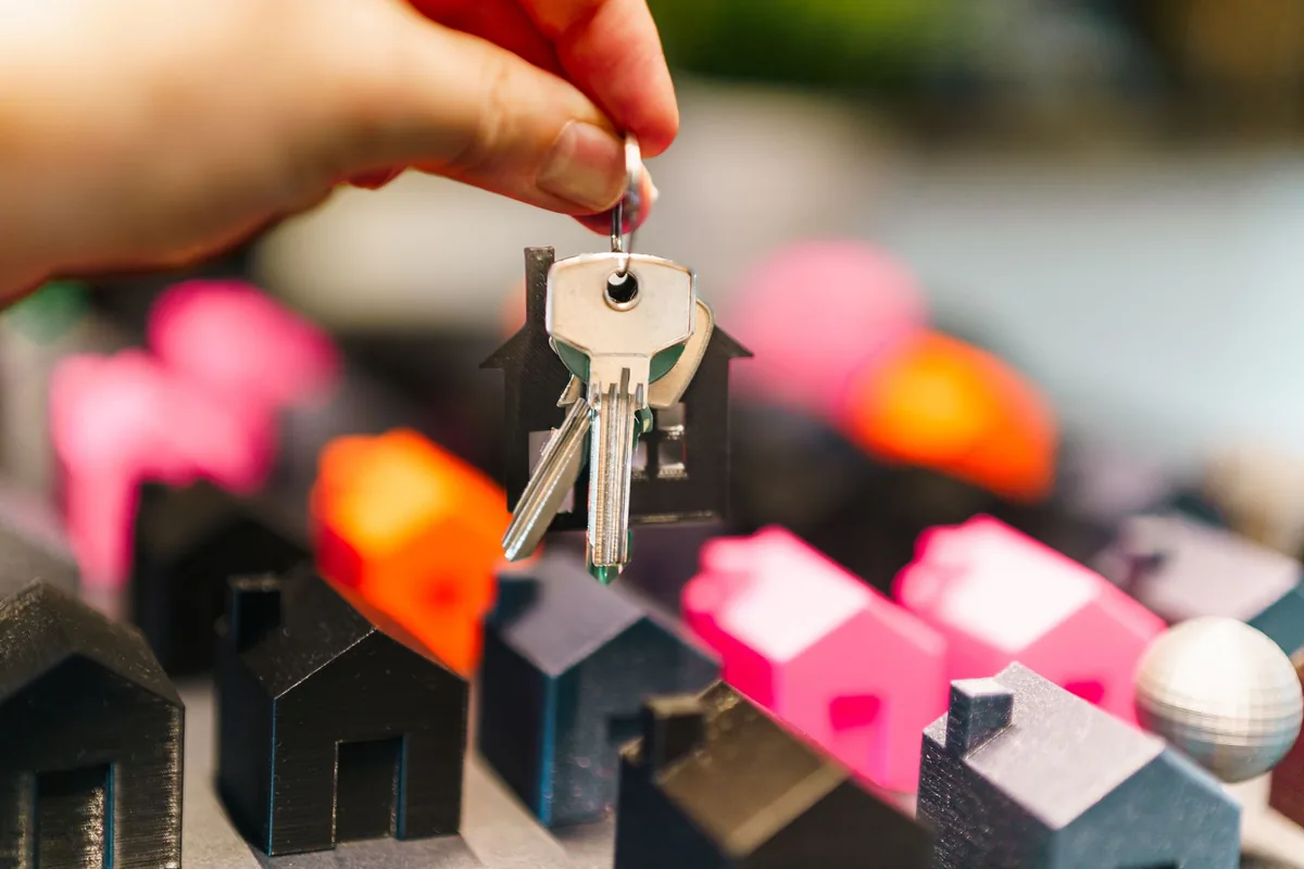 Mano que sostiene unas llaves con un llavero en forma de casa entre casas en miniatura de colores