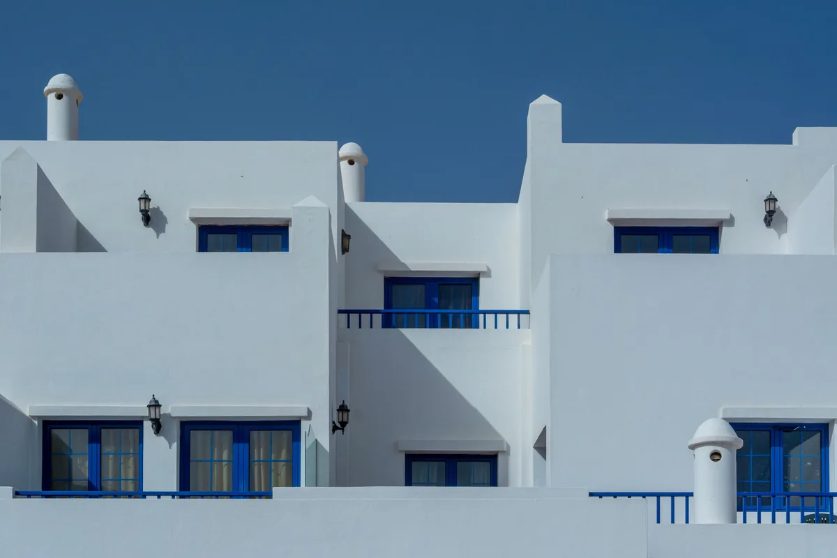 Edificio de apartamentos blancos de estilo canario con ventanas y barandillas azules, chimeneas redondas y terrazas de techo plano