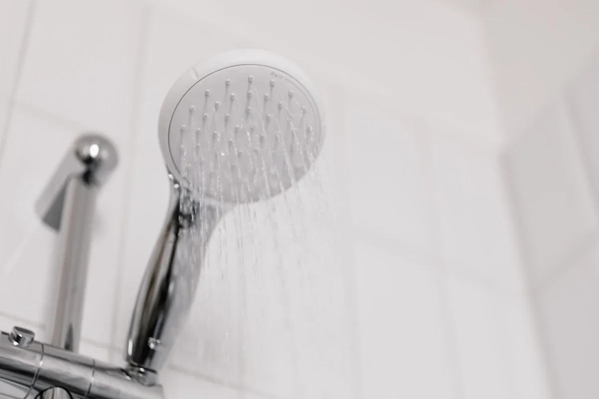 Alcachofa de ducha blanca con el agua cayendo sobre azulejos blancos