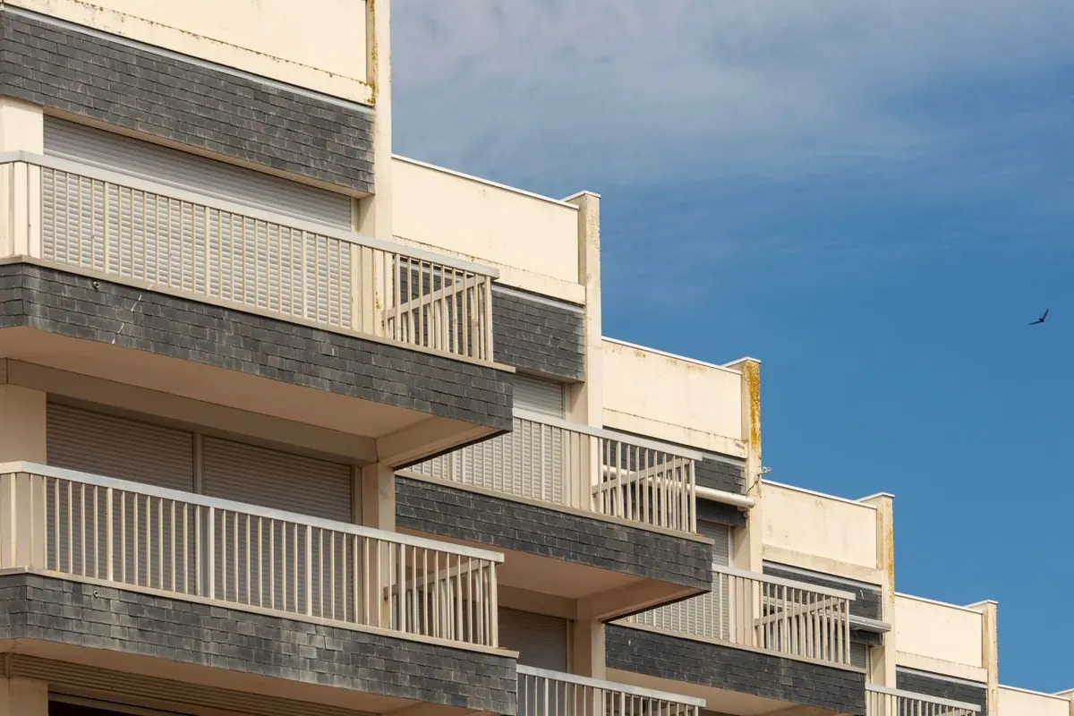 Fachada de un edificio de apartamentos con balcones escalonados de barandilla blanca bajo un cielo azul