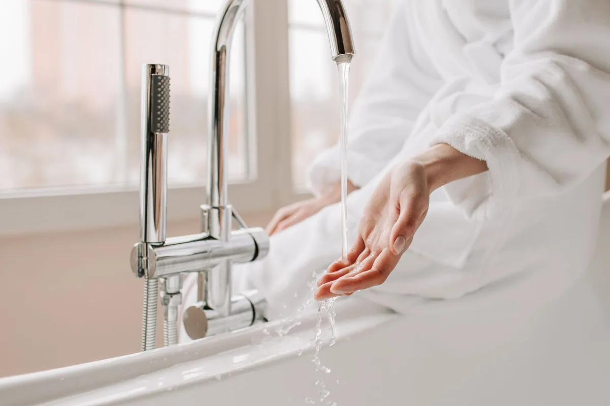 Mano comprobando el agua que cae de un grifo cromado de bañera